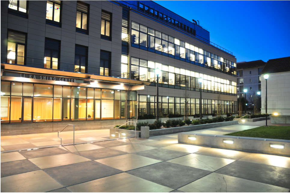 Building lit by warm light in the foreground and cool lights in the background above a courtyard of large checkered squares.