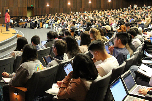 A lecture hall full of students watching a presenter on stage.