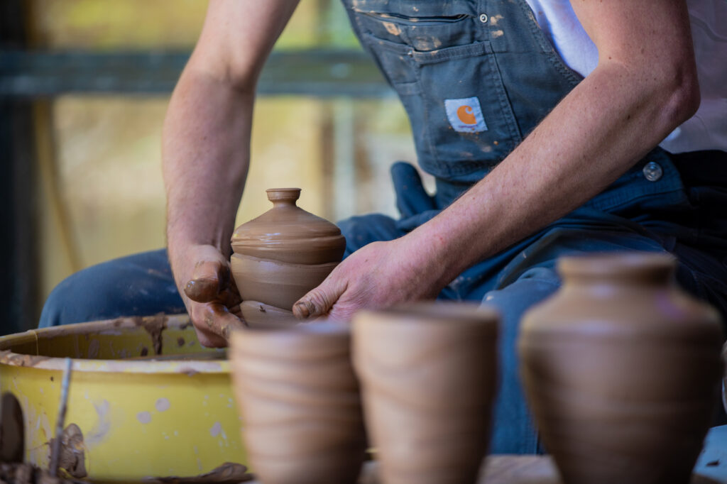 A person molding clay on a pottery wheel into a vase-like figure.