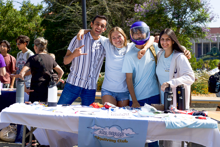 Four students, including Ashley Lee (middle left), table at Calapalooza on Sproul for their Air Bears club. One student wears a skydiving helmet.