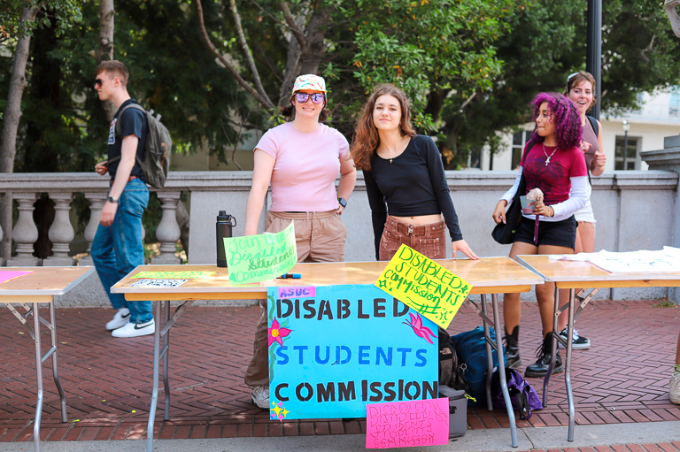 Shelby Suppiger and Carlyn Leavitt table at Calapalooza for the Disabled Students Commission. Their sign boasts four colorful signs, all reading "Disabled Students Commission."