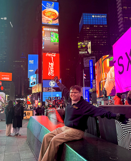 Rico sitting on a bench in New York. Neon signs illuminate the background.