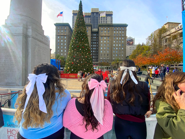 A photo taken from the back of Deborah and two friends in gazing at a Christmas tree.