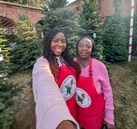 A selfie of Daniella and a relative volunteering at a Christmas tree lot. The pair wear red work aprons.