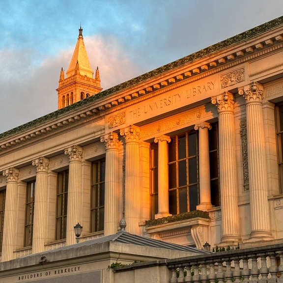 The University Library bathed in golden light, just as the sun is setting. The sky is blue and spotted with clouds.