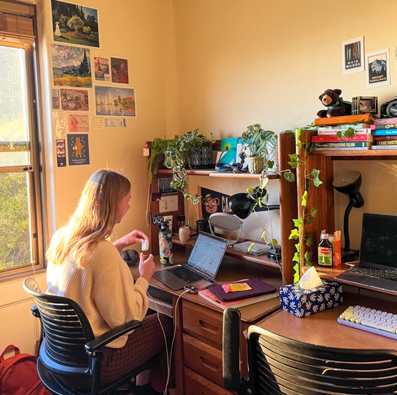 Inside of I-House Dorm. A student sits at their decorated desk in a yellow room. 