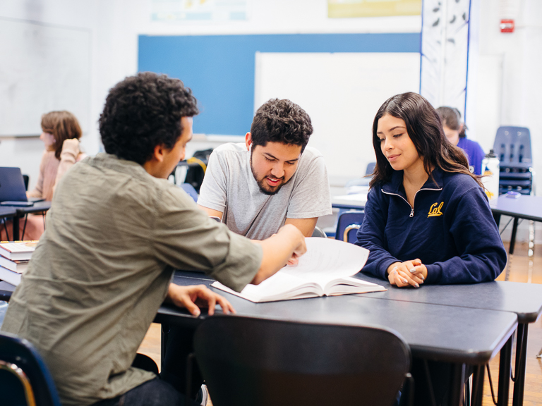 Three Cal students sit at a desk, flipping through a book together.