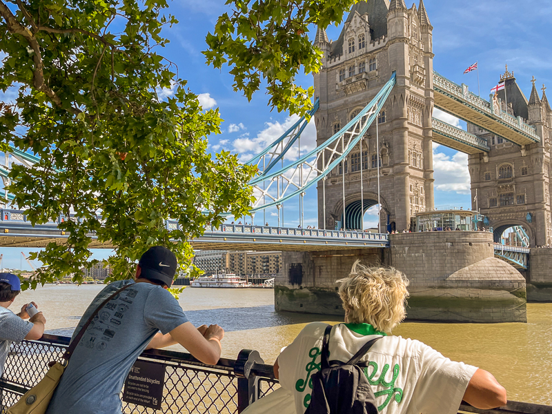 Students standing at a railing looking across a river at Tower Bridge in London.